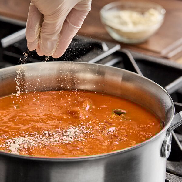 A gloved hand sprinkling Hometown Provisions Onion Powder over a pot of food.