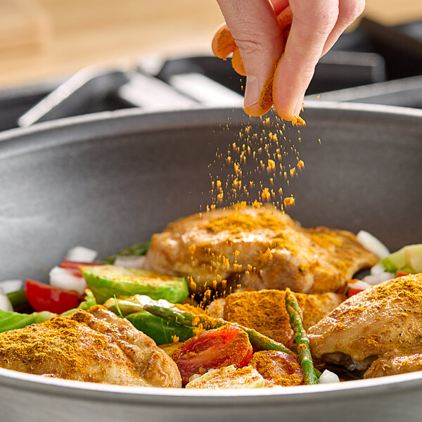 A person sprinkling Hometown Provisions ground turmeric on a pan of food.