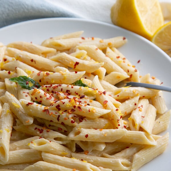 A plate of pasta with a fork and lemon slices on the side.