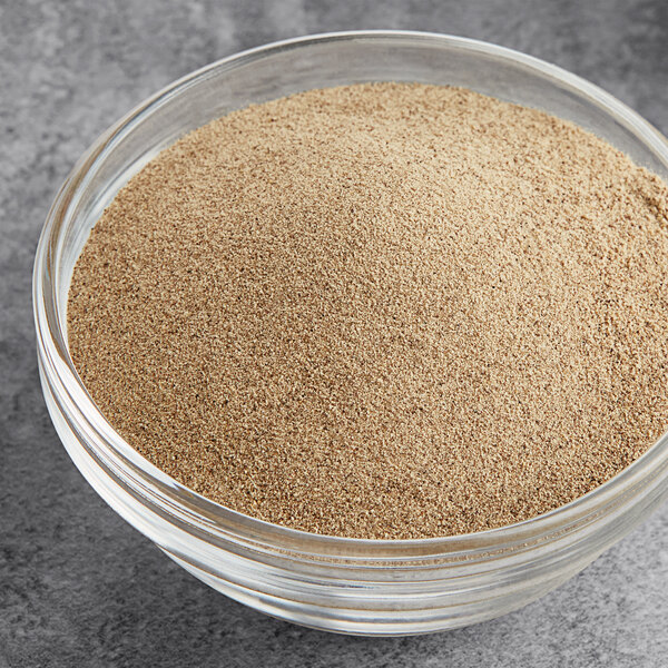 A bowl of fine ground white pepper on a grey surface.