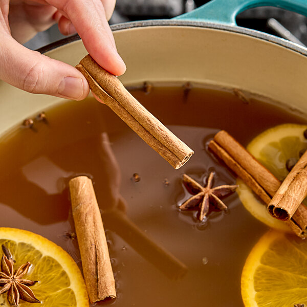 A person holding Hometown Provisions cinnamon sticks over a pot of brown liquid.