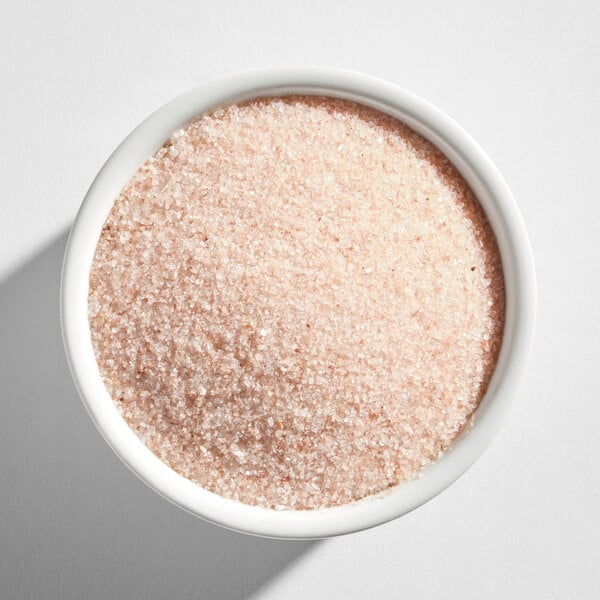 A white bowl filled with fine, light pink granules resembling Himalayan salt.