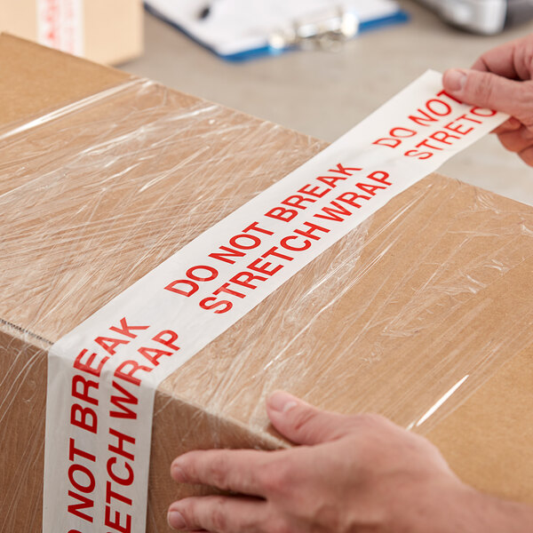 A person using Tape Logic "Do Not Break Stretch Wrap" to seal a box.