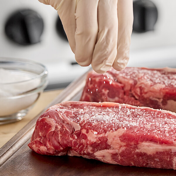 A hand sprinkling Hometown Provisions Coarse Sea Salt on a piece of raw meat.