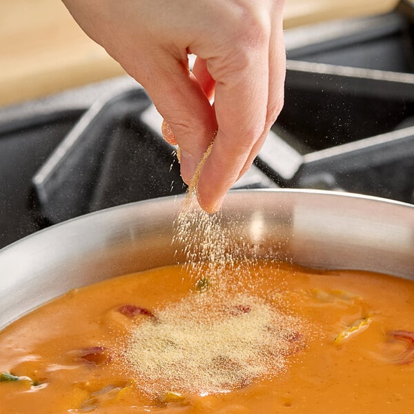 A person sprinkling granulated garlic into a bowl of soup.