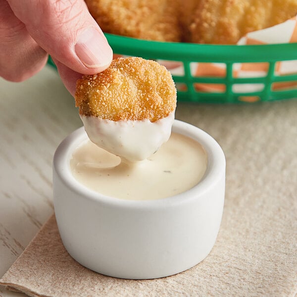 A hand holding a fried chicken piece being dipped into white sauce.