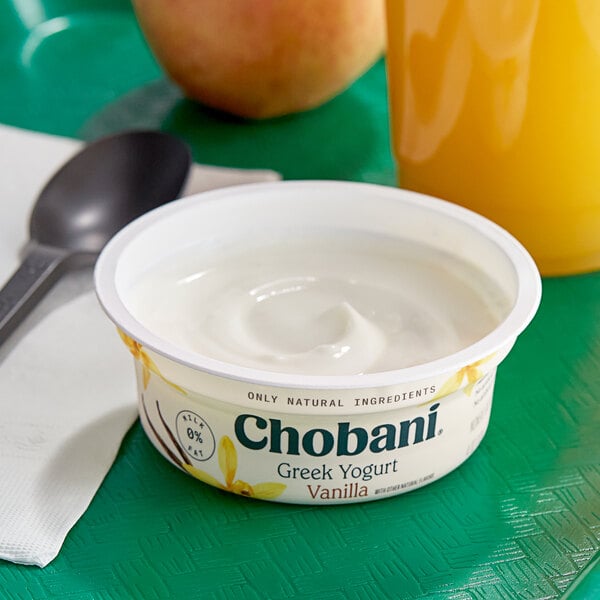 A container of Chobani non-fat vanilla Greek yogurt with a spoon and a bowl of yogurt.