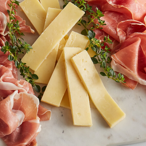 A Collier's Powerful Welsh Cheddar cheese wedge on a cutting board with cheese, ham, and herbs.