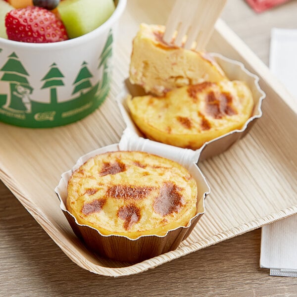 A tray with Artisan Kitchens Bacon and Three Cheese Egg Bites and a bowl of fruit on a table.