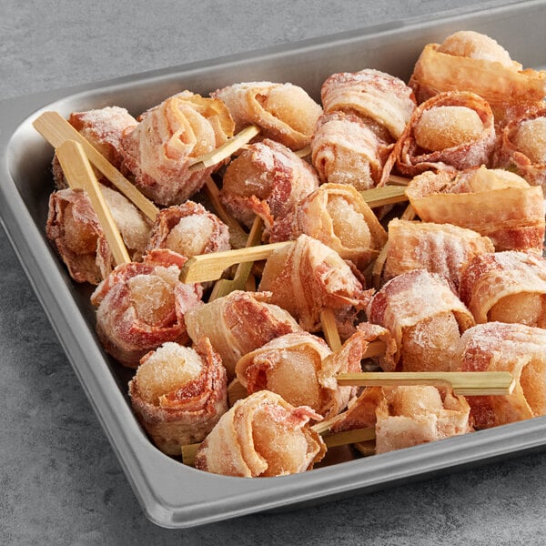 Cuisine Innovations bacon wrapped water chestnuts on sticks on a tray.