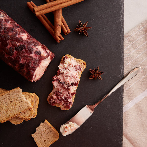 A piece of bread with Celebrity Goat Cranberry Cinnamon Chevre spread on it next to a knife.