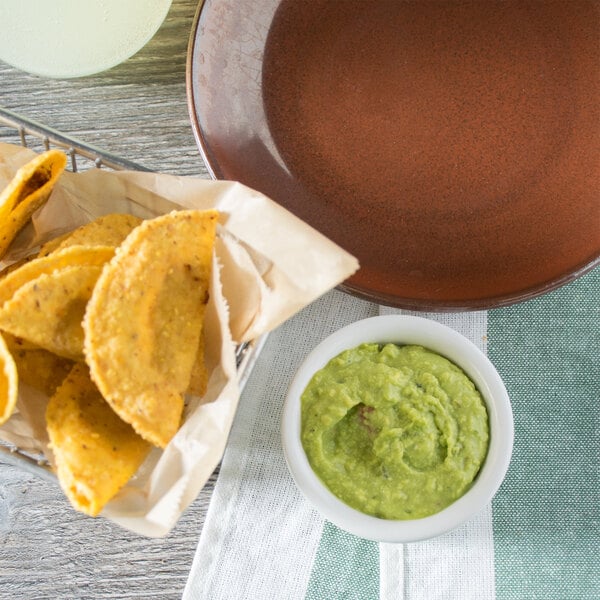 A brown plate of tortillas with a bowl of Calavo guacamole on a table.