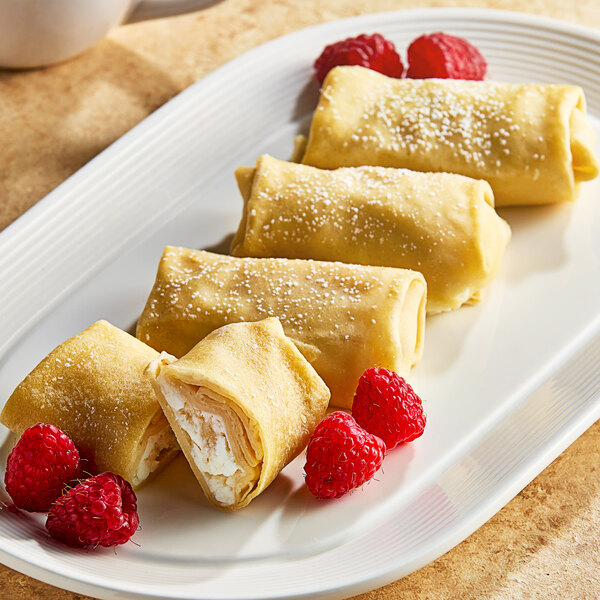 A white plate with Cuisine Innovations Cheese Blintzes, raspberries, and crepes.