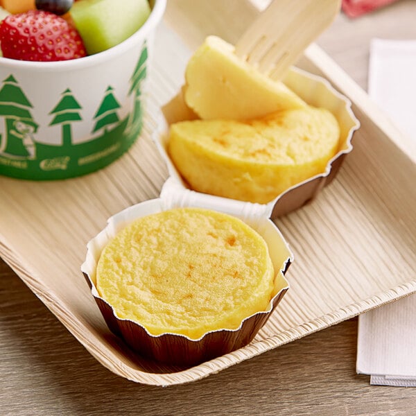 A white tray with two Artisan Kitchens Three Cheese Egg Bites and a cup of fruit.