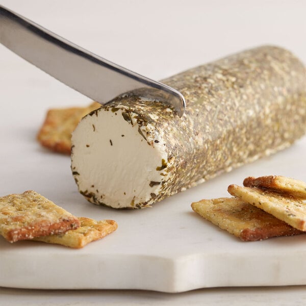 A knife cutting a block of Celebrity Goat Garlic and Herb Goat Cheese.
