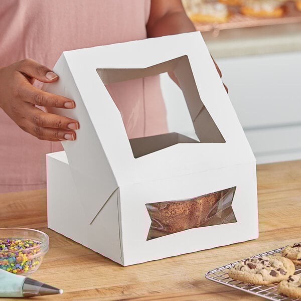 A woman holding a white Southern Champion bakery box with a plastic window containing a cookie.