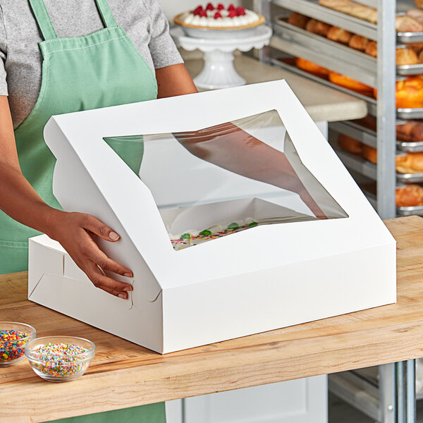 A woman holding a white Southern Champion Bakery Box with a clear plastic window.