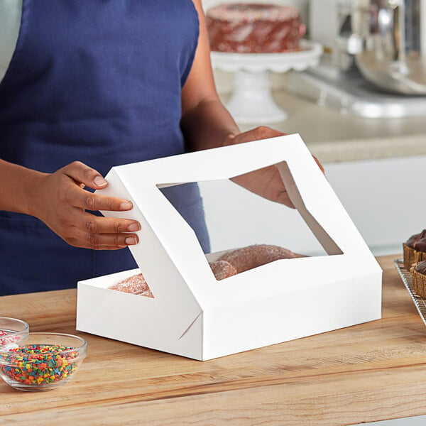 A woman holding a Southern Champion white bakery box with a donut inside.