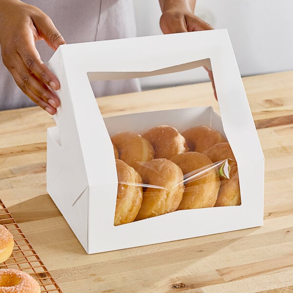 A person holding a Southern Champion white bakery box filled with donuts.