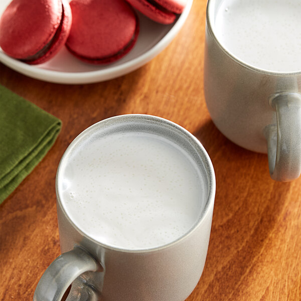 A close-up of a white mug of Cocoa Classics Arctic White Chocolate cocoa mix with a plate of cookies.