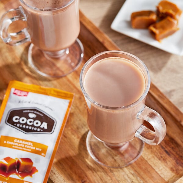 A glass mug of Cocoa Classics hot chocolate and a packet of caramel candies on a tray.