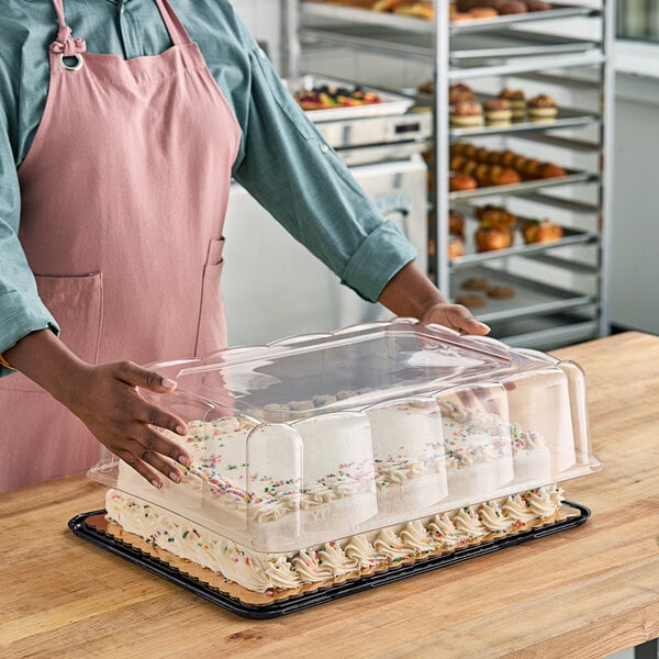 A woman holding a cake in a D&W Fine Pack plastic container with a clear scalloped lid.