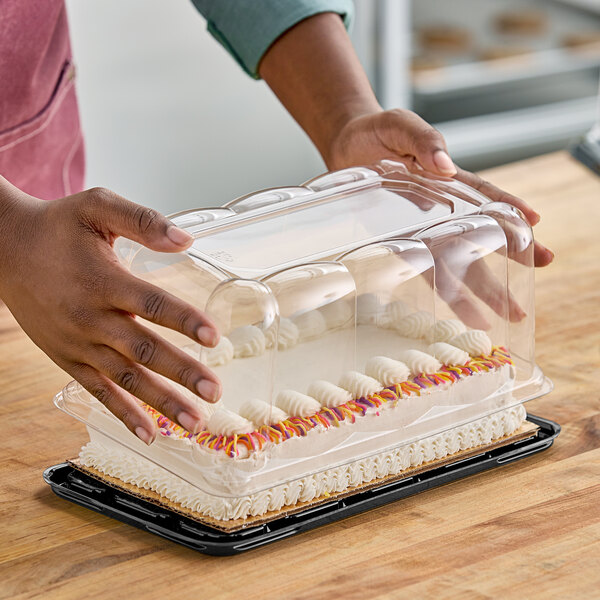 A person holding a cake in a clear plastic container with a scalloped dome lid.