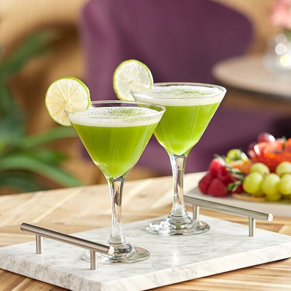A tray with two glasses of green liquid with lime wedges on a table.