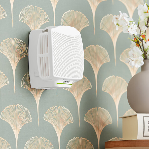 A white square Oxy-Gen Powered Oxygen-Pro air freshener system on a wall.