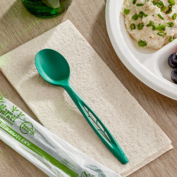 A Stalk Market green compostable spoon on a table next to a bowl of mashed potatoes.