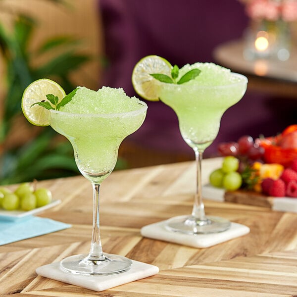 Two glasses of green Primor Guanabana puree drink with a lime and mint garnish on a table.