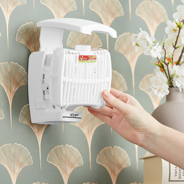 A hand holding a white Oxy-Gen air freshener refill.