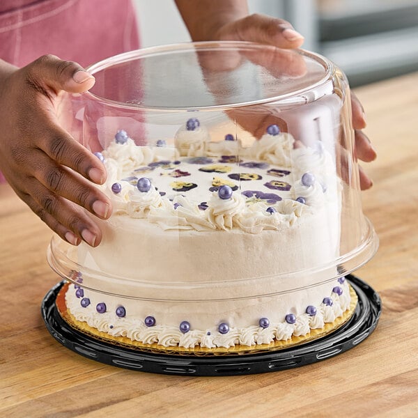 A person holding a cake in a D&W Fine Pack plastic display container.