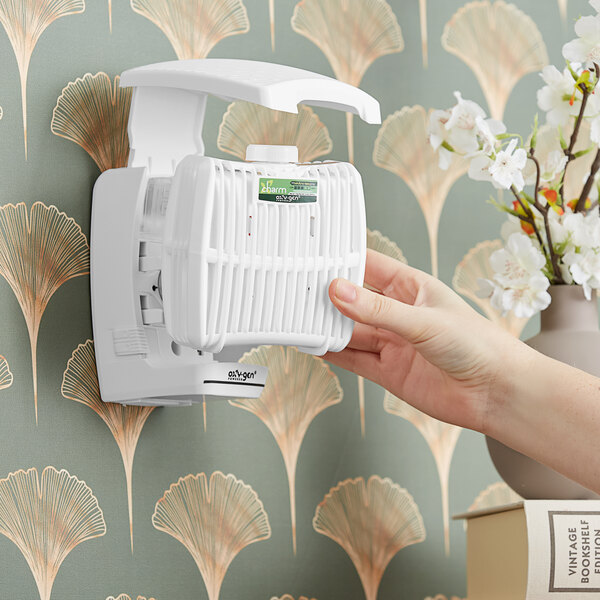 A hand replacing a white Oxy-Gen air freshener cartridge in a white device.