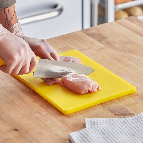 A person cutting raw chicken on a yellow Choice cutting board.