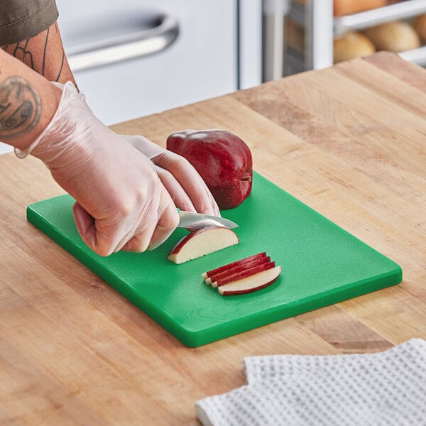 A hand slicing a red apple on a green Choice polyethylene cutting board.