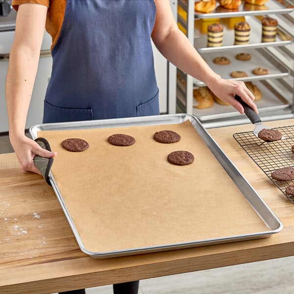 A woman in a blue apron using Baker's Lane unbleached parchment paper to remove cookies from a sheet pan.