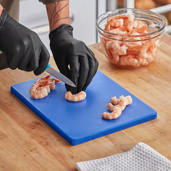 A person in black gloves cutting shrimp on a blue Choice cutting board.