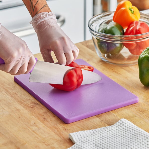 A person cutting a red pepper on a purple Choice cutting board.