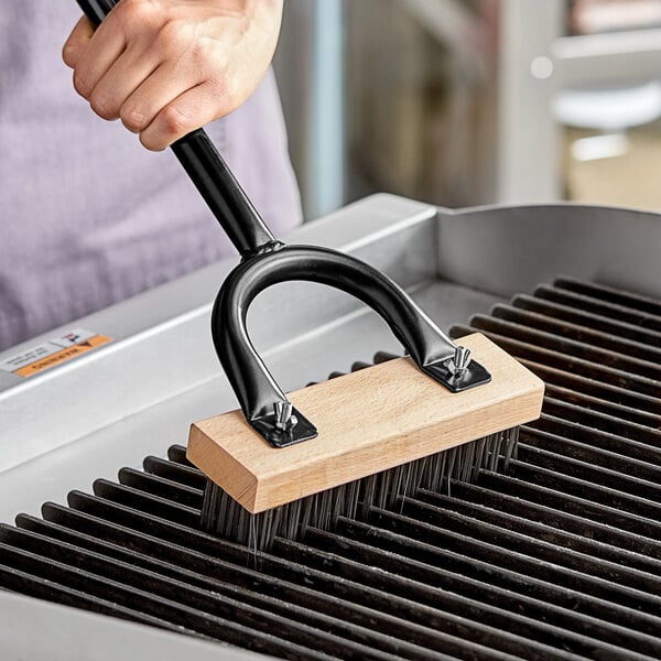 A person using a Choice medium carbon steel bristle brush head to clean a grill.