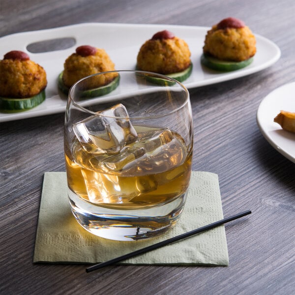 A Reserve by Libbey Symmetry rocks glass of liquid with ice on a table next to appetizers.
