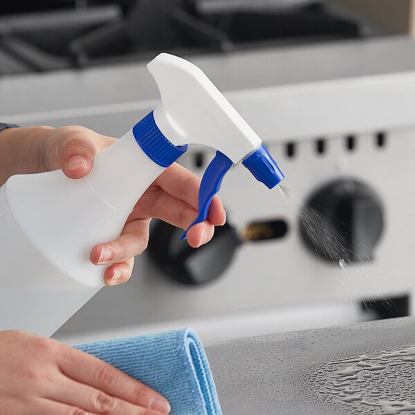 A hand holding a Lavex blue plastic spray bottle spraying a counter