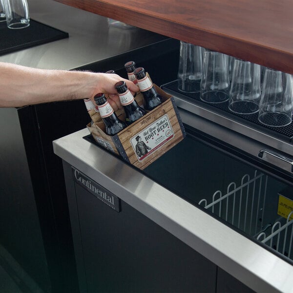 A hand holding a bottle of beer in a Continental Refrigerator bottle cooler.