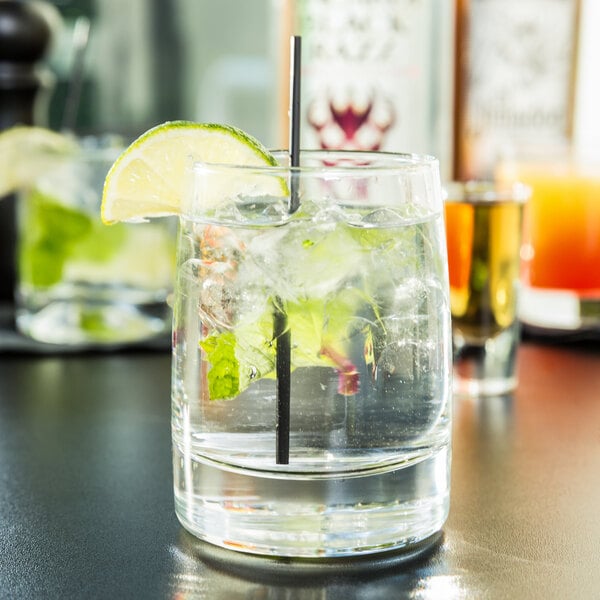 A Libbey rocks glass with a straw and a lime wedge on a table.