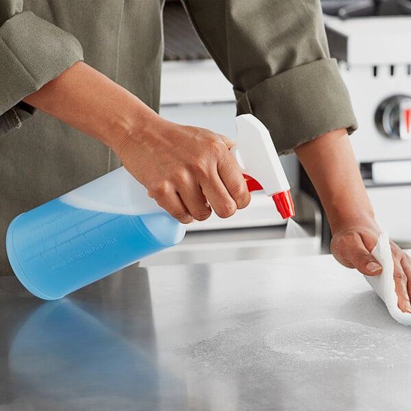 A person cleaning a counter with a Lavex red plastic spray bottle filled with blue liquid.