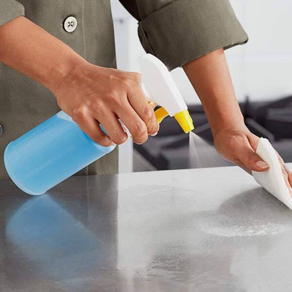 A person using a Lavex yellow spray bottle to clean a metal counter.