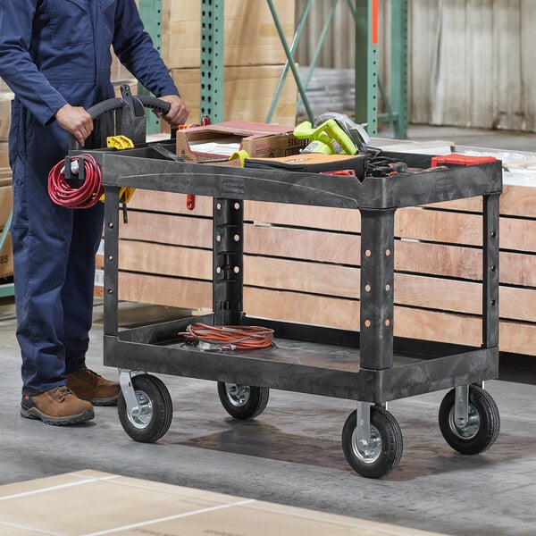 A man in a blue jumpsuit using a Rubbermaid utility cart to transport a box of wires.