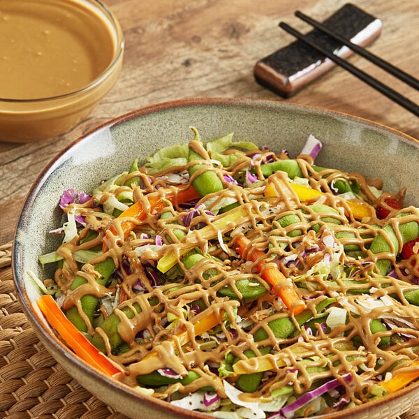 A bowl of salad with sunflower butter sauce and chopsticks.