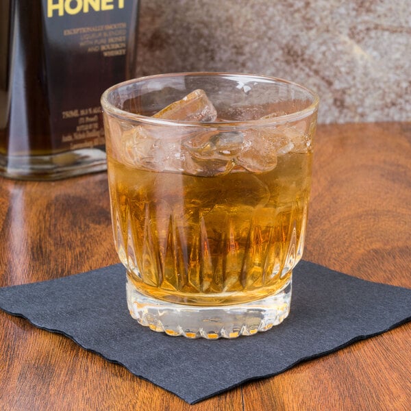 A Libbey Winchester Rocks glass with whiskey and ice on a napkin next to a bottle of liquor.