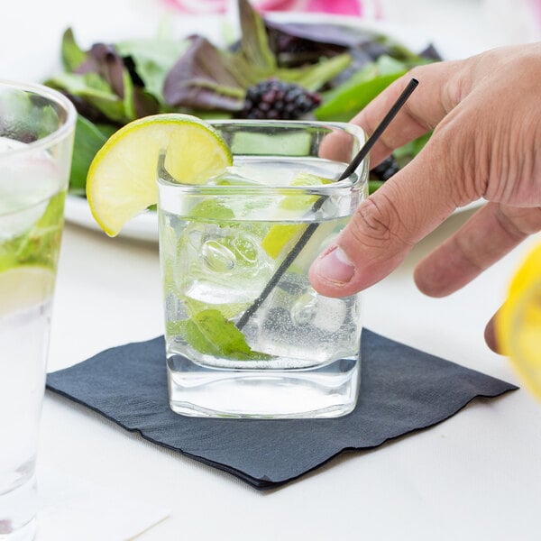A hand holding a Libbey Rocks glass of water with ice and lime slices.